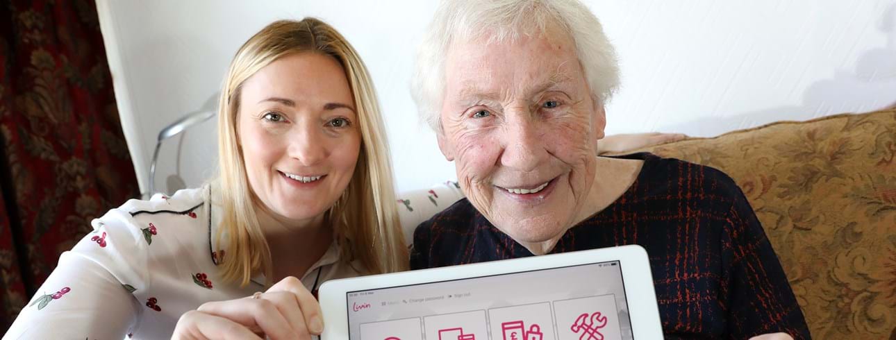 An elderly woman with Roslyn Littledyke, Head of Customer Experience and Service Improvement, accessing the tenant app on her tablet