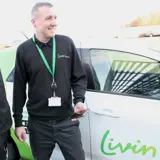 Gas engineer in Livin works uniform holding his mobile phone standing next to his work van 