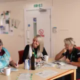 Community craft sessions with three ladies chatting around a table 